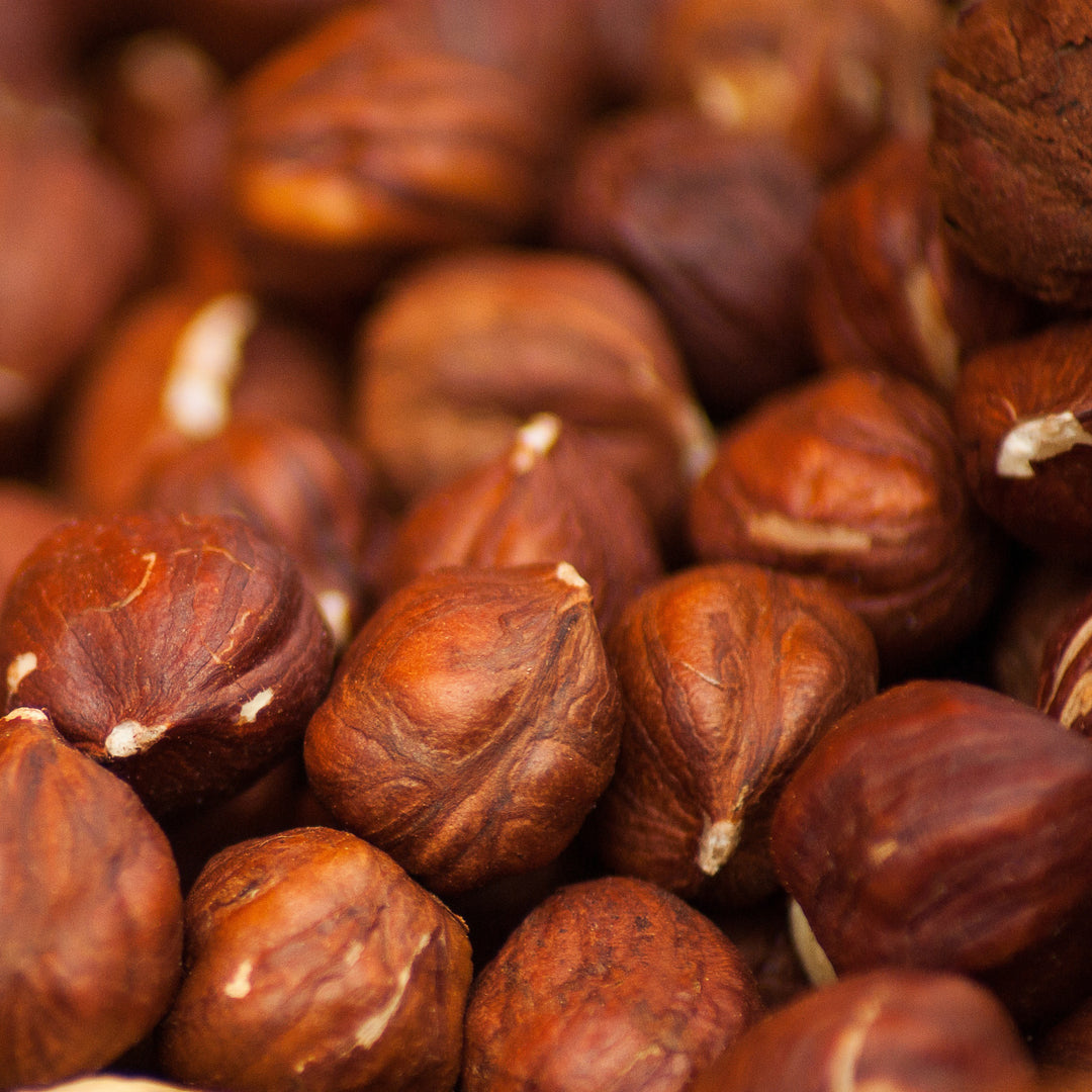A close-up pile of browned hazelnuts with textured, wrinkled skins showing natural beige nubs.