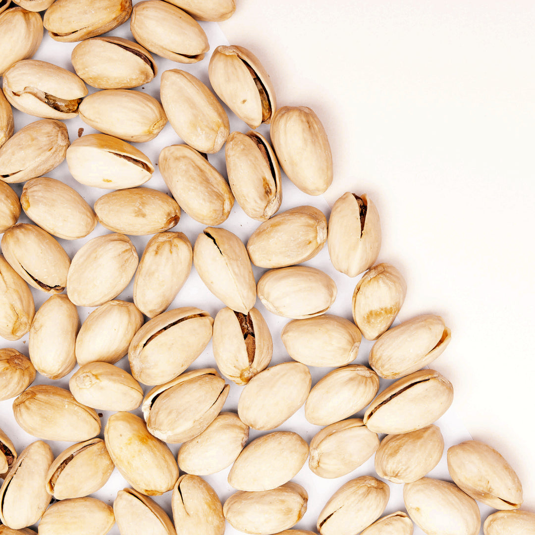 A close-up top-down view of pistachios in their shells scattered across a white background.