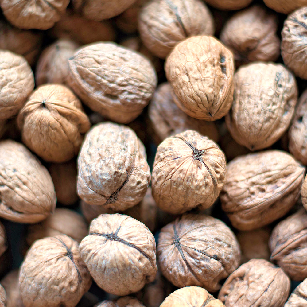 A close-up pile of whole walnuts with textured brown and beige shells filling the frame.