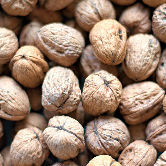 A close-up pile of whole walnuts with textured brown and beige shells filling the frame.